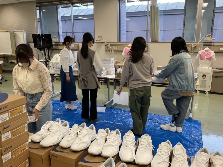 ユニフォーム試着会で、学生たちが白い靴を試着しながら準備を進めている様子。