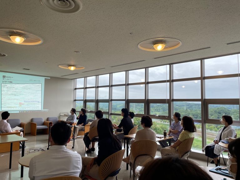 学術委員会企画の「Myプレミアムを語る会」が開催され、参加者がプレゼンテーションを聴いている様子。窓からは緑豊かな景色が見える。