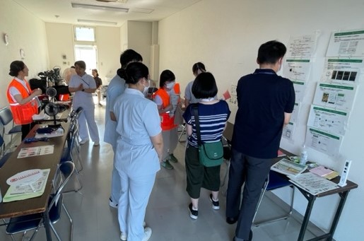 住民を対象とした健康相談の準備中、保健師からアプリの説明を受ける学生たち。