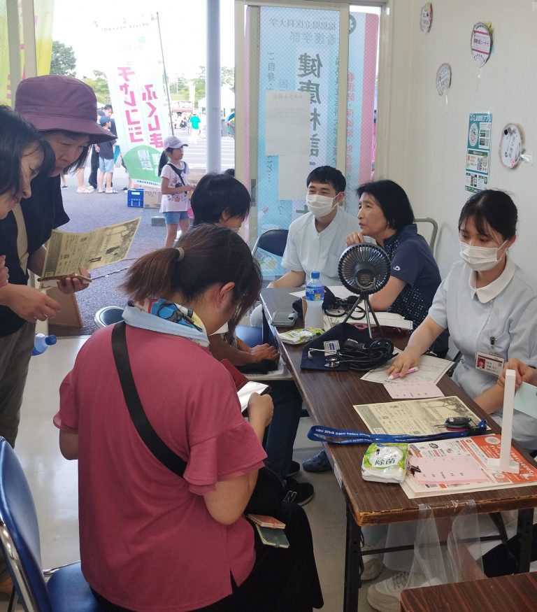 住民を対象とした健康相談の様子。学生たちが笑顔で対応し、参加者とコミュニケーションを取っている。