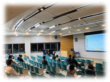学術交流推進小委員会主催の会議が行われている教室の様子。参加者が座ってプレゼンテーションを聴いている。