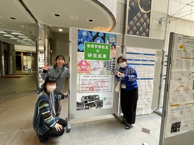 看護学部の教員が研究成果を発表するポスターの前でポーズをとる3人の女性。