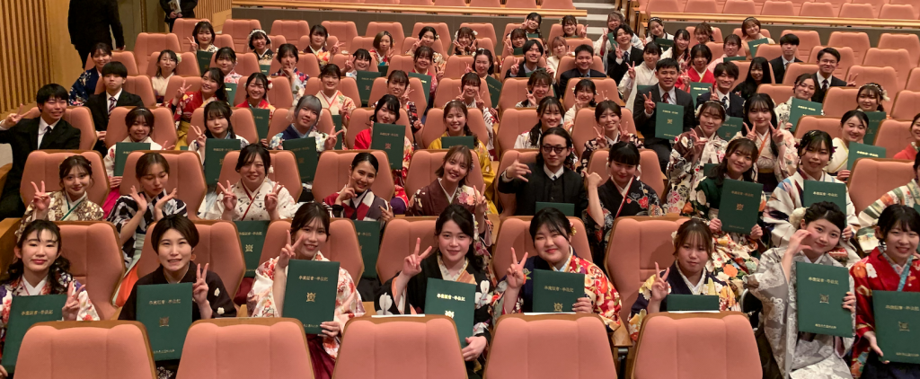 学位記授与式で卒業生たちが笑顔で記念撮影をしている様子。着物を着た学生たちが卒業証書を持ち、喜びを表現しています。