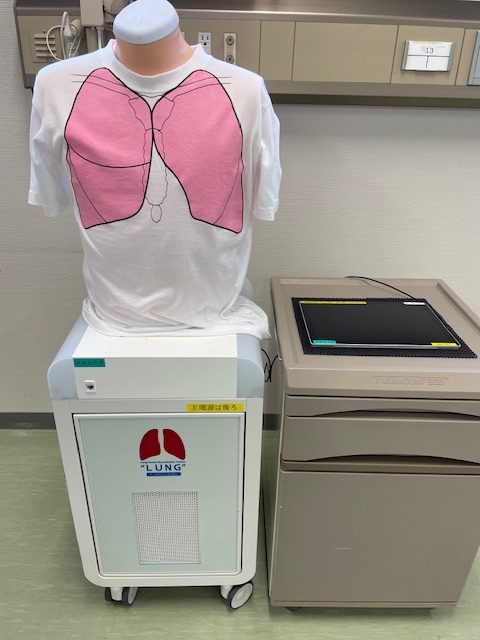白いTシャツにピンクの肺のイラストが描かれ、医療機器の横に置かれている様子。