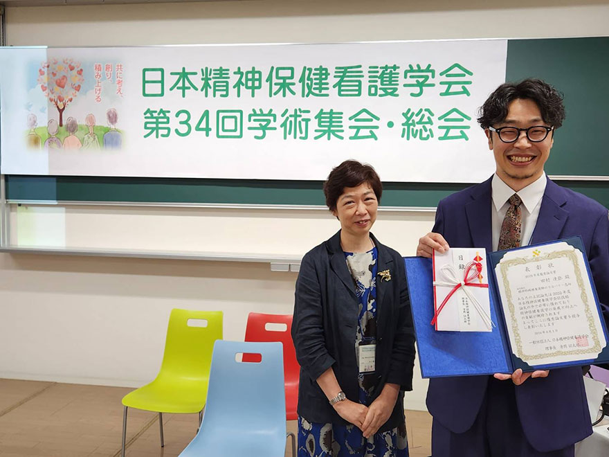 田村達弥先生が日本精神保健看護学会第34回学術集会で優秀論文賞を受賞し、隣に大川貴子先生が立っています。