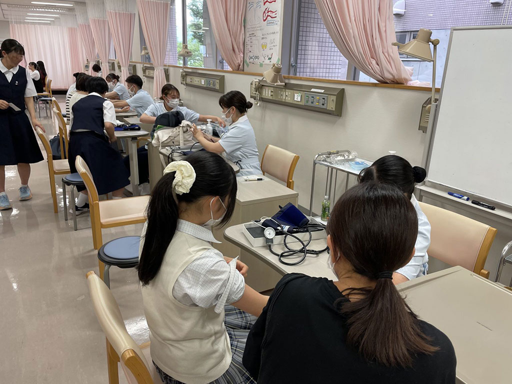 看護学部のオープンキャンパスで、来校者に血圧測定を行う学生たちの様子。