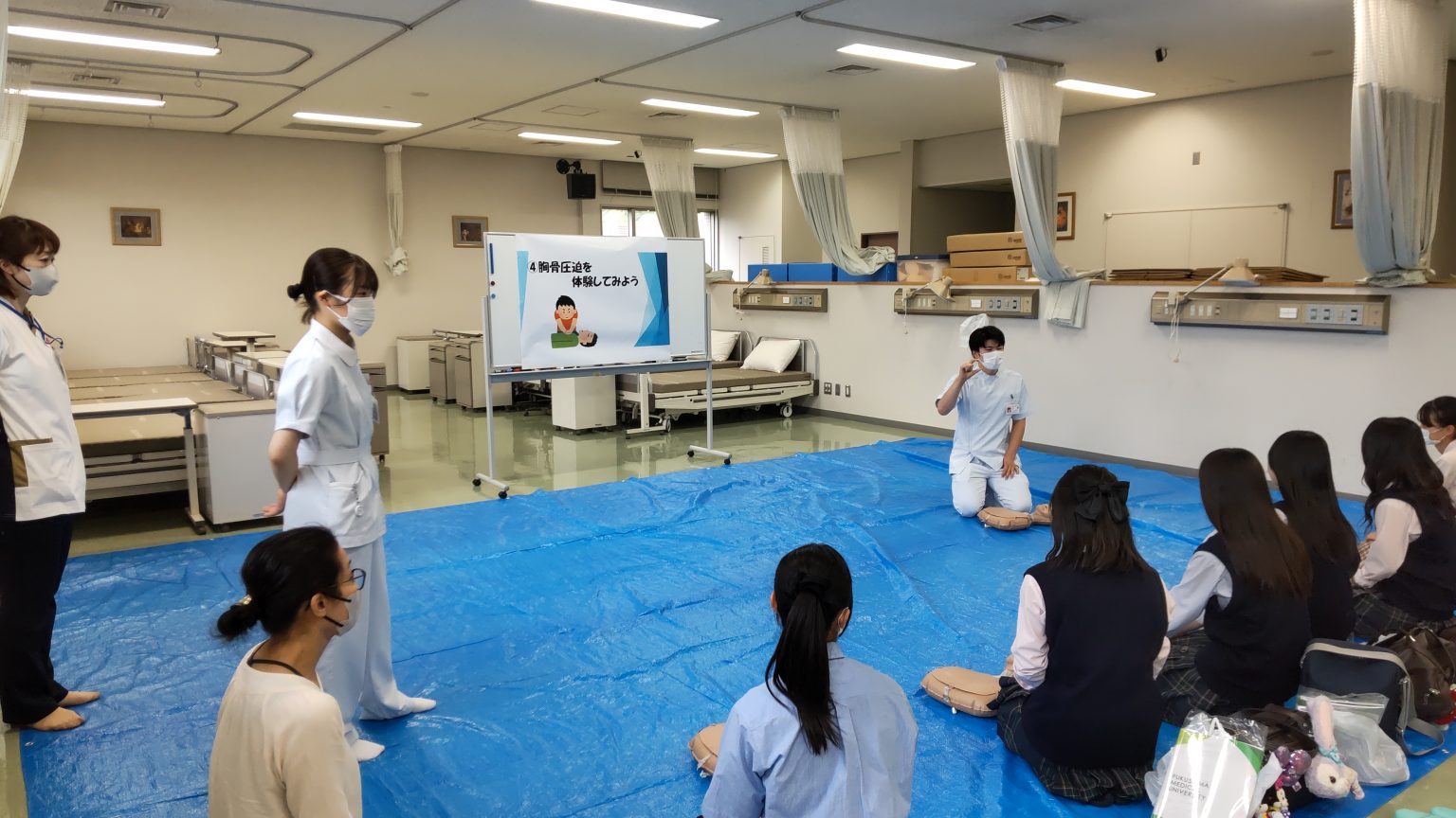 胸骨圧迫体験コーナーで高校生に説明する看護学部の学生たち。