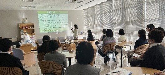 研究発表会で講演を行う女性と、参加者たちが聴講している様子。