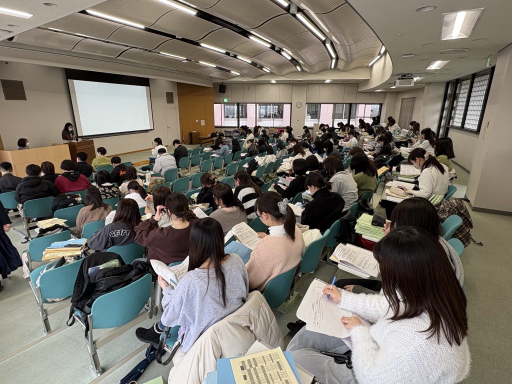 新年度の講義を受ける学生たちが真剣な表情でノートを取っている教室の様子。