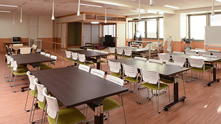 A spacious workshop room with multiple tables and chairs, designed for everyday life activities.