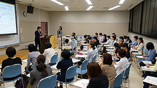 Training session for health professionals, featuring a speaker and an engaged audience in a classroom setting.