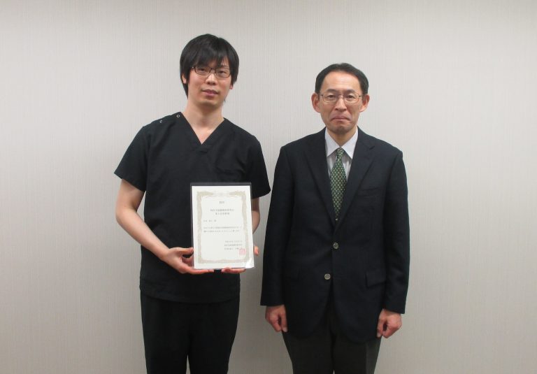 第8回核医学画像解析研究会で菅野賞を受賞した右近直之助教と受賞証書を持つ姿。