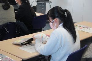 中高生がふくしま国際医療科学センターで見学会に参加し、資料を読みながらメモを取っている様子。