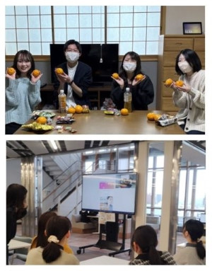 FMU保健科学部カフェで、学生たちがオレンジを持ちながら楽しそうに交流している様子。上部にはプレゼンテーション用のモニターが映っている。