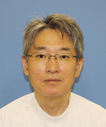 今坂堅一教授のポートレート。白衣を着て、眼鏡をかけた中年男性が青い背景の前で微笑んでいる。