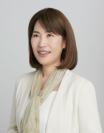 小川真里子教授が微笑みながら白いジャケットとスカーフを着用しているポートレート。
