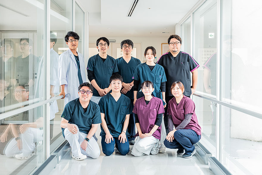 病院の廊下で、9人の医療スタッフが笑顔で並んでいる様子。
