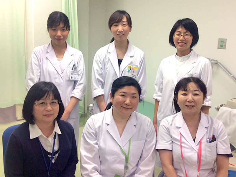 白衣を着た6人の医療従事者が室内で微笑んでポーズを取っている。医療現場のチームワークを示す。