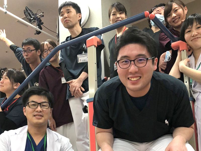 職員が笑顔で階段に集まっている。仲間との親しみやかさと協力を示している。