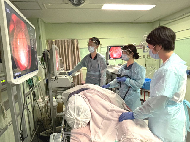 医療スタッフが内視鏡検査を行う様子。モニターには体内の映像が映し出され、複数のスタッフが検査を支えている。