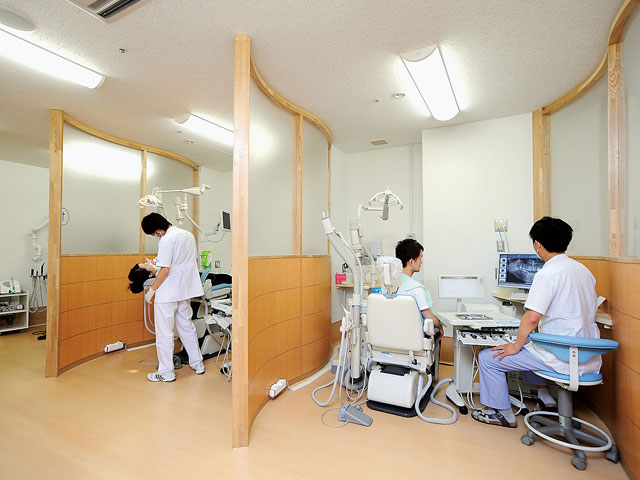 歯科口腔外科の診察室で、医療スタッフが患者の治療を行い、歯科用モニターで画像を確認している様子。