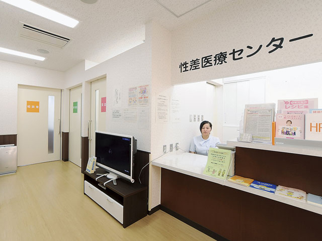 医療センターの受付に座る職員と、壁に貼られた案内やパンフレットが並ぶ静かな待合室の様子。