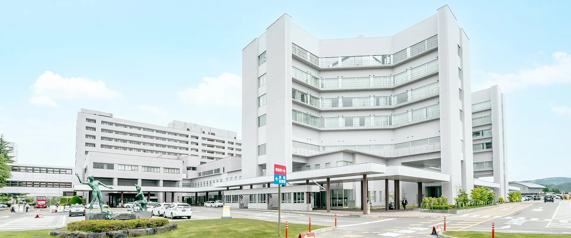 福島県立医科大学附属病院の外観、白い建物と広い駐車場が見える。