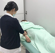 看護師がベッドに横たわる患者の腕を優しく触れながらケアをしている医療現場の様子。