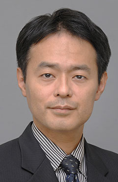 主任教授の島袋充生氏のポートレート写真。ビジネススーツを着用し、真剣な表情でカメラを見つめている。