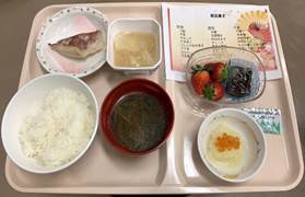 栄養管理部の食事トレイに盛り付けられた、白ご飯、味噌汁、焼き魚、デザートのいちごとプリンが並ぶ食事の様子。