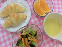 朝食のテーブルに並んだクロワッサン、サラダ、オレンジ、飲み物が盛り付けられた様子。