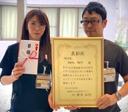 福島医大の栄養管理部が受賞した賞状を持つ2人のスタッフが写っている写真。