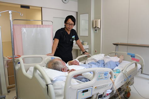 病室で患者に寄り添う医療スタッフが、食事サポートを行っている様子。