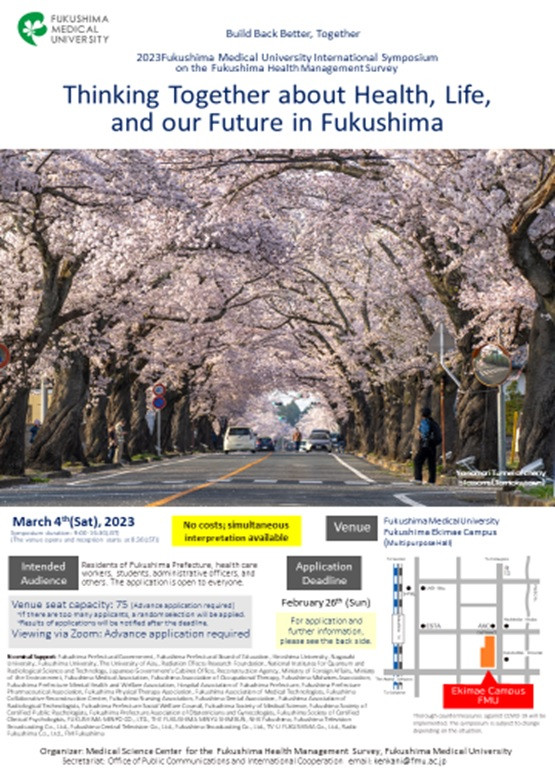 Cherry blossom trees lining a street, with a banner for a symposium on health and future in Fukushima.