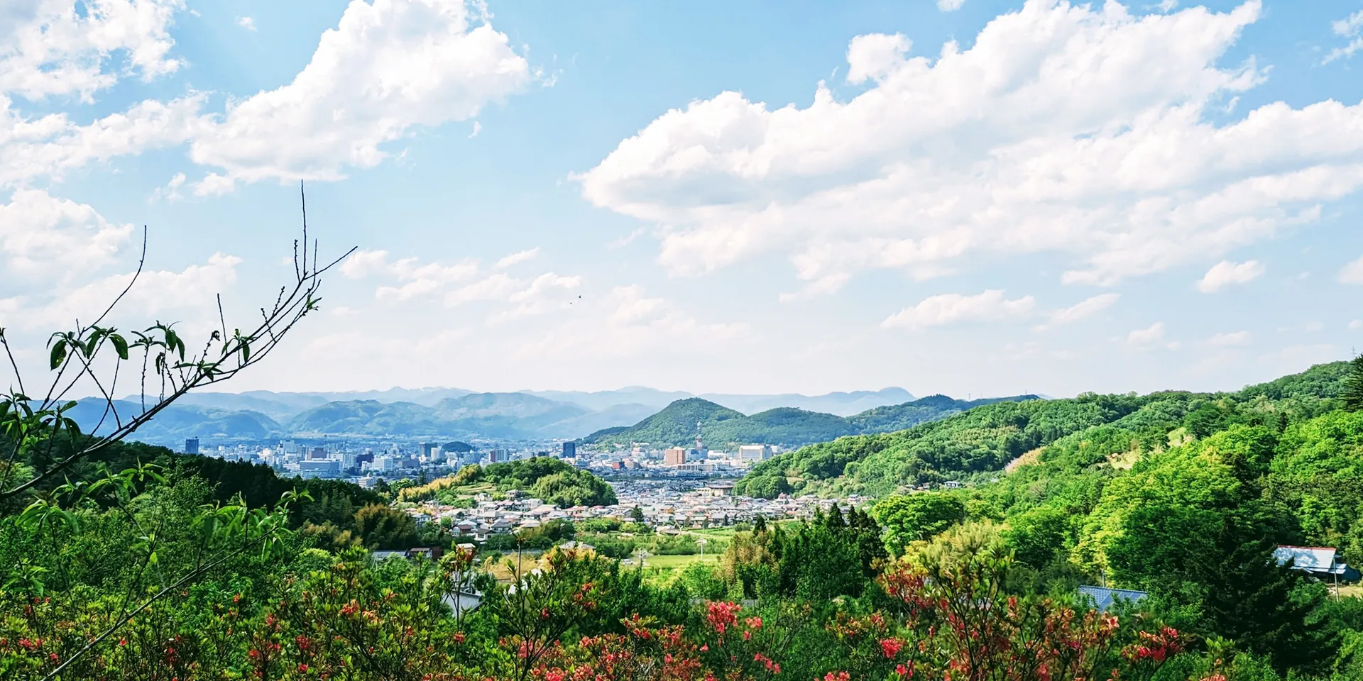 福島県の緑豊かな山々と青空を背景にした風景、遠くに市街地が見える。