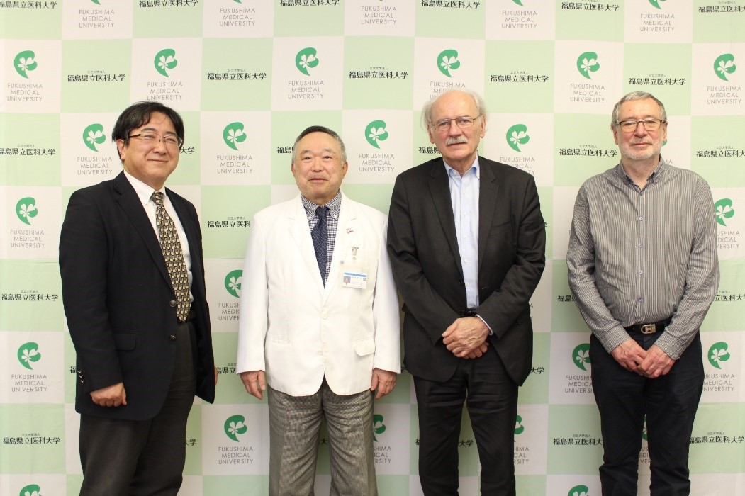 四人の男性が並んで立っている。背景には「福島県立医科大学」のロゴが繰り返し表示されたパネルがある。