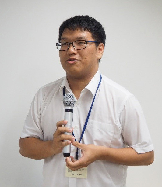 清潔な白いシャツを着た人物が、マイクを持って話している様子。背景はシンプルな白。