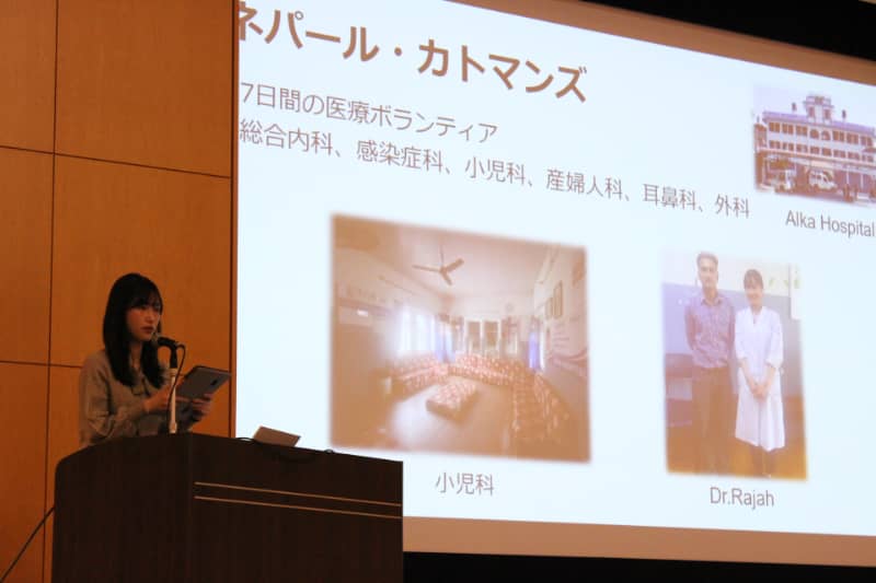 講義室でプレゼンテーションを行う女性の前に、大きなスクリーンにネパールの医療ボランティアに関する情報が表示されている。