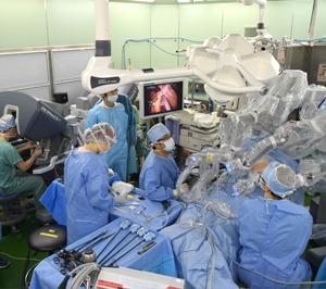 手術室でロボット支援手術を行う医療チーム。全員が手術着と帽子を着用し、集中して作業に取り組む。