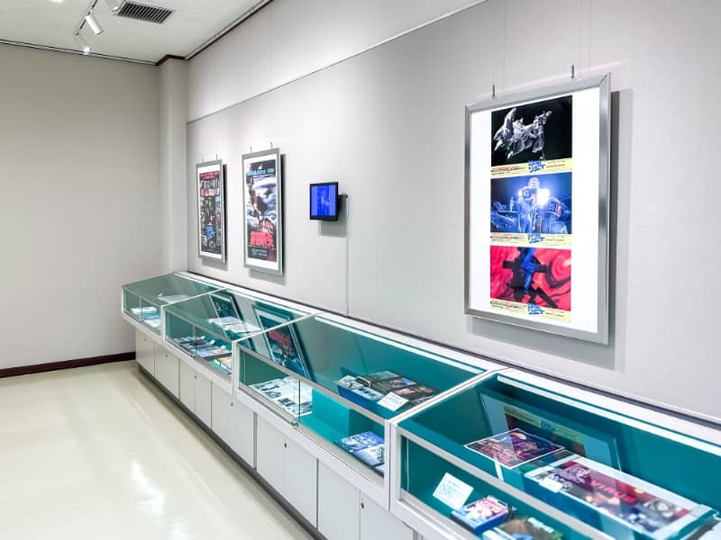 展示室内には、壁に掛けられたポスターとガラスケース内にさまざまなアイテムが展示されています。