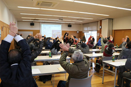参加者が笑いヨガを実践し、手を挙げている講演会の様子。健康促進と認知症予防を目的とした活動。
