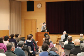 健康長寿に関する講演会で話す教授と聴衆の様子。