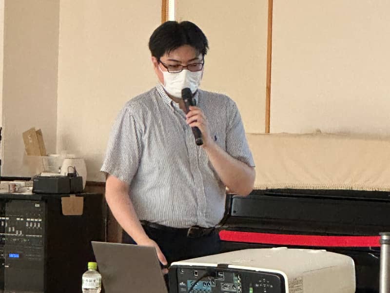 健康づくりに関する講演を行う男性がマイクを持ち、プレゼンテーションをしている様子。