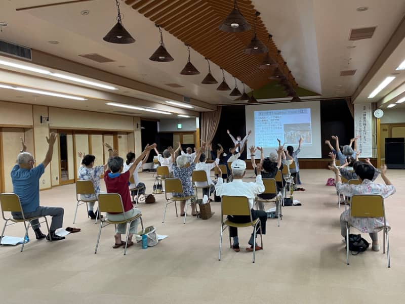 高齢者が笑いヨガを実践している様子。参加者全員が手を挙げて笑い、健康促進を目指している。