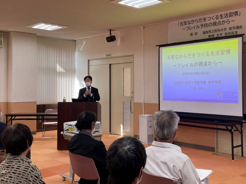 講演会で話す大平哲也教授と聴衆の様子、テーマは「元気なからだをつくる生活習慣」。