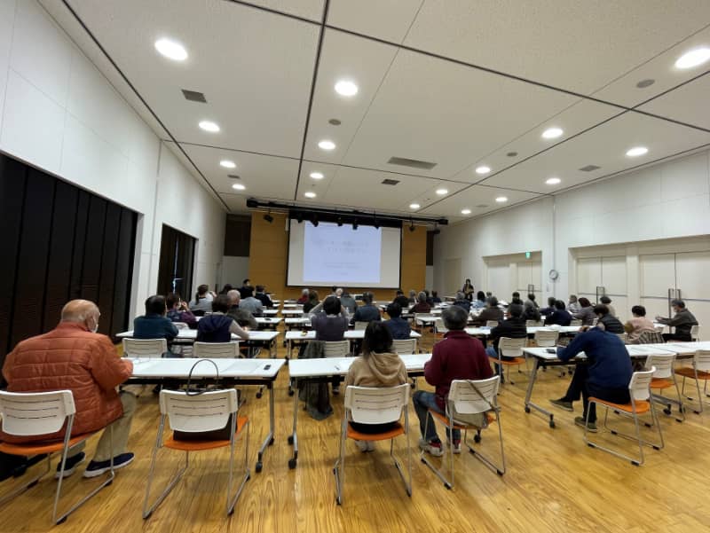 会場で講演を聴く参加者たちが座っている様子。前方にはスクリーンが設置されている。