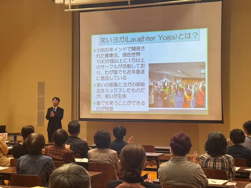 笑いヨガの講演中、参加者が手を挙げて笑いの体操を実践している様子。