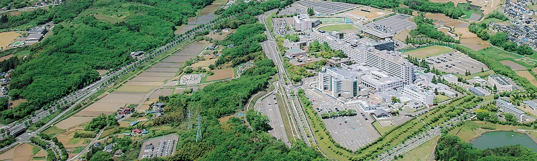福島県立医科大学の周辺風景、緑豊かな環境と医療施設が広がる空撮画像。