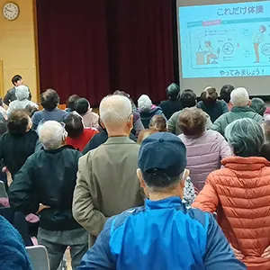 地域の健康づくりを目的とした講演会で、参加者が体操を行っている様子。