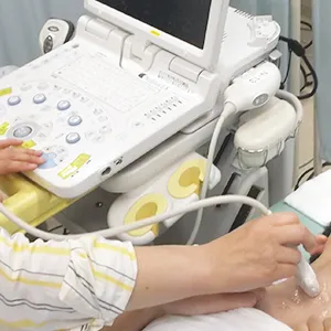医療機器の超音波検査を行っている様子。患者の肌にプローブを当て、検査を進める医療従事者の手が見える。